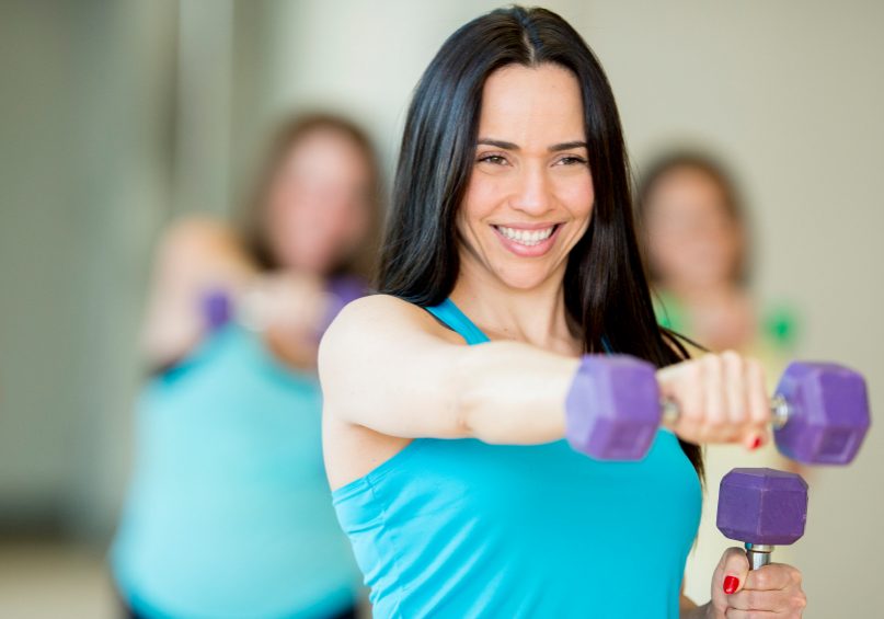 A group of female friends exercising with free weights in a health club, following an instructor.